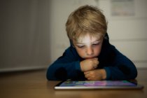 Маленький мальчик смотрит мультики с цифровым планшетом на деревянном полу — стоковое фото