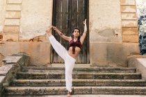 Frau, die von Hand bis Fuß auf Stufen in der Nähe des Eingangs eines antiken Gebäudes steht und Yoga macht — Stockfoto