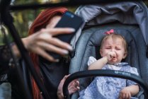 Madre mostrando smartphone al bambino scontento nel passeggino — Foto stock