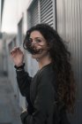 Side view of attractive young female with curly hair looking at camera while standing on city street on windy day — Stock Photo