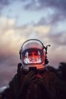 Female astronaut in illuminated vintage helmet with mobile phone standing in nature at sunset — Stock Photo