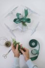 Mains masculines décorant drone enveloppé comme cadeau de Noël avec branche de sapin et ruban vert sur fond blanc — Photo de stock