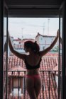 Jovem mulher em lingerie posando na varanda com vista para telhados antigos — Fotografia de Stock