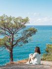 Woman sitting on cliff at blue seaside and looking at view — Stock Photo