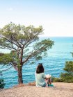 Femme assise sur une falaise au bord de la mer bleue et regardant la vue — Photo de stock