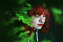 Young red haired woman between fir twigs on black background — Stock Photo