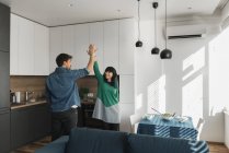 Jovem alegre e mulher dando mais cinco uns aos outros enquanto estão na cozinha moderna juntos — Fotografia de Stock