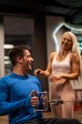 Man doing exercise in gym with woman standing and smiling — Stock Photo