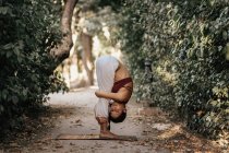 Flexión delgada mujer mientras hace yoga en el callejón en el parque de otoño - foto de stock