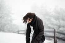 Seitenansicht der jungen Frau in warmer Kleidung zu Fuß in der Nähe von Zaun an windigen Wintertag in herrlicher Landschaft — Stockfoto