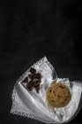 Galleta de chocolate con trozos de chocolate sobre servilleta blanca sobre fondo negro - foto de stock
