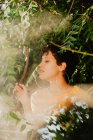 Portrait de femme brune sensuelle aux cheveux courts debout dans la brume dans la végétation verte avec la lumière du soleil — Photo de stock