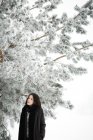 Mulher muito jovem em roupa elegante olhando para longe, enquanto de pé perto da árvore coberta de neve no dia frio no campo maravilhoso — Fotografia de Stock