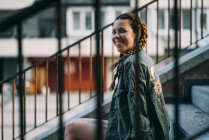 Усміхнена руда дівчина з косами, що сидить на сходах у місті — стокове фото