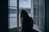 Frau blickt durch Zimmerfenster — Stockfoto