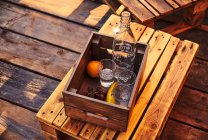 De cima vista de três copos com garrafa e uvas com banana e laranja deitado em caixa de madeira na cadeira — Fotografia de Stock