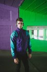 Giovane bell'uomo in giacca sportiva con auricolare in piedi su sfondo di parete colorata e guardando la fotocamera — Foto stock