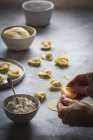 Human hands folding dough with stuffing of cottage cheese preparing delicious tortellini — Stock Photo