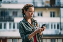 Nachdenkliches rothaariges Mädchen mit Zöpfen mit Handy gegen Wohnhaus — Stockfoto