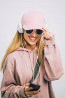 Mulher elegante com capuz rosa e boné ouvindo música com fones de ouvido — Fotografia de Stock