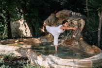 Женщина, стоящая в фонтанной воде в дереве, позирует во время занятий йогой в парке — стоковое фото