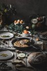 Вид вкусной тортильи на сковороде у плиты со слайсами, помидорами, фруктами, орехами и листьями на деревянной доске — стоковое фото