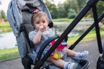 Дитяча дівчинка смокче великий палець в колясці в парку — стокове фото