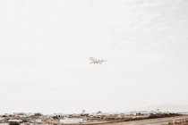 From below view of white aircraft flying in cloudy sky over town in Mykonos, Greece — Stock Photo