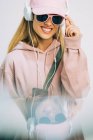 Stylish woman in pink hoodie and cap listening to music with headphones — Stock Photo