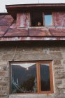 De baixo tiro de macho olhando para fora janela de cabana resistida em pequeno assentamento na Bulgária, Balcãs — Fotografia de Stock
