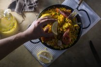 Menschliche Hand, die Zitrone über die traditionelle spanische Paella marinera mit Reis, Garnelen, Tintenfisch und Muscheln in der Pfanne drückt — Stockfoto