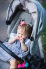 Cute baby girl eating cookie in stroller outdoors — Stock Photo
