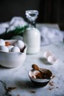 Bowl and spoon of cocoa powder standing on marble tabletop near bowl of fresh eggs and bottle of nice dairy — Stock Photo