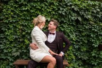 Захоплений чоловік і жінка носять модні весільні костюми і дивляться один на одного проти зеленого живоплоту — стокове фото