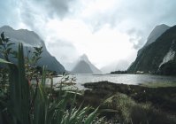 Nubes gruesas flotando sobre montañas increíbles y aguas tranquilas en un magnífico día en el Parque Nacional Fiordland en Nueva Zelanda - foto de stock