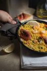 Людська рука тримає сковороду традиційної іспанської паелья марина з рисом, креветками, кальмарами та мідіями — стокове фото