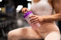 Hands of sportswoman holding drinking bottle in gym — Stock Photo