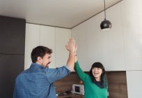 Веселий молодий чоловік і жінка дарують високі п'ять один одному, стоячи на сучасній кухні разом — стокове фото