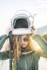 Mulher confiante em traje de astronauta colocando no capacete à luz do sol — Fotografia de Stock