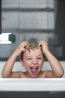 Портрет игривого маленького мальчика, сидящего в ванной — стоковое фото