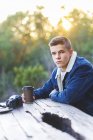 Portrait of teenage boy sitting at table outdoors with coffee cup and photo camera — Stock Photo