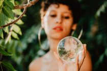 Jovem morena topless segurando bola transparente de vidro em madeiras verdes — Fotografia de Stock