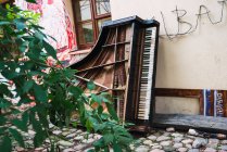 Старое сломанное фортепиано возле здания на каменном тротуаре маленькой городской улицы — стоковое фото