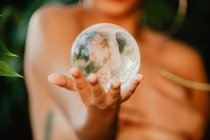 Jovem morena topless segurando bola transparente de vidro em madeiras verdes — Fotografia de Stock