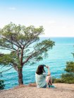 Женщина сидит на скале голубого моря и держит солнцезащитные очки — стоковое фото