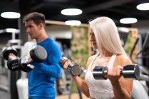 Atlético hombre y mujer haciendo ejercicio con mancuernas en el gimnasio - foto de stock
