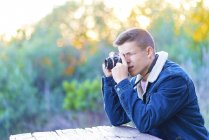 Молодой человек сидит за столом на улице с фотокамерой — стоковое фото