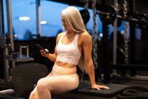 Женщина сидит в спортзале и пользуется мобильным телефоном — стоковое фото