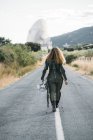 Visão traseira da mulher vestindo traje de astronauta andando ao longo da estrada rural — Fotografia de Stock