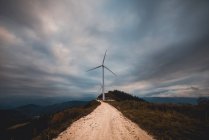 Row of modern windmills standing on side of narrow countryside road on cloudy day — Stock Photo